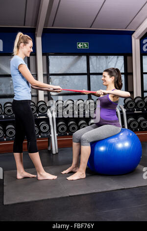 Pregnant woman doing some exercising helped by trainer Stock Photo