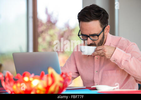 Focused man drinking coffee while using laptop Stock Photo