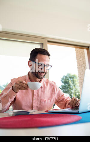 Man having coffee while using laptop Stock Photo