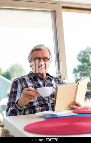 Old man having coffee while reading Stock Photo