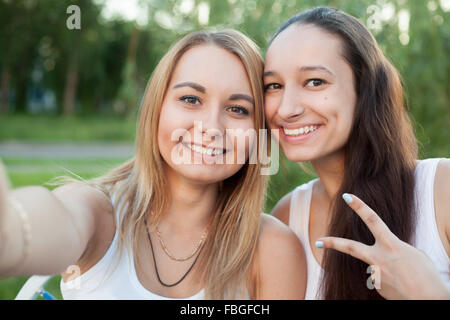 Two happy smiling beautiful blond and brunette young women friends taking playful selfie picture together, showing peace sign at Stock Photo