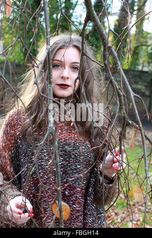 Beautiful modern young woman looking through branches Stock Photo