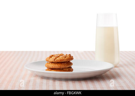 Stack of three homemade peanut butter cookies on white ceramic plate and glass of milk on classic checkered table Stock Photo