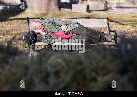 Sofia, Bulgaria - January 14, 2016: Homeless man is sleeping on a bench in Sofia. Bulgaria is EU's poorest country. Stock Photo