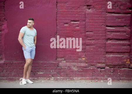 Portrait of confident serious hot guy wearing casual clothing walking on the street beside old red brick wall, looking back, cop Stock Photo