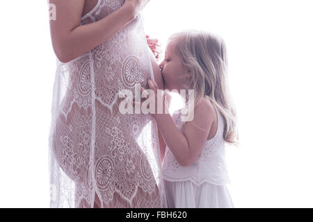 Cute little girl kissing mothers pregnant belly. Bump shoot in lace. Pregnant woman and daughter.  Babies sister bw Stock Photo