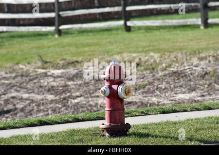 A rusty fire hydrant next to a sidewalk, grass, fence. Stock Photo