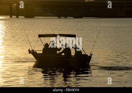Three silhouetted men and one woman going early morning fishing in a small runabout dinghy metal boat on the Shoalhaven River in Nowra Stock Photo