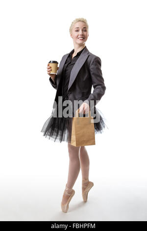 Studio shot of a ballerina model holding a takeaway cup in her right hand and a paperbag in her left hand whilst en pointe. Stock Photo