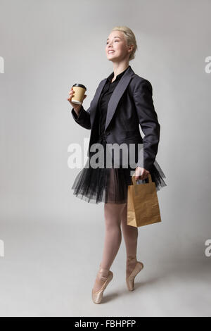 Studio shot of a ballerina model holding a takeaway cup in her right hand and a paperbag in her left hand whilst en pointe. Stock Photo