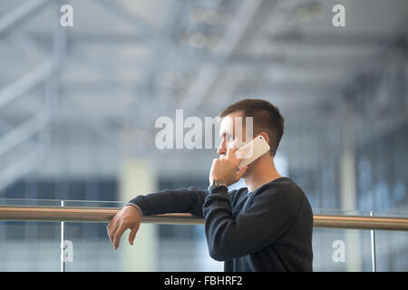 Portrait of young man in 20s talking on mobile phone in modern building, wearing jersey, side view, copy space Stock Photo