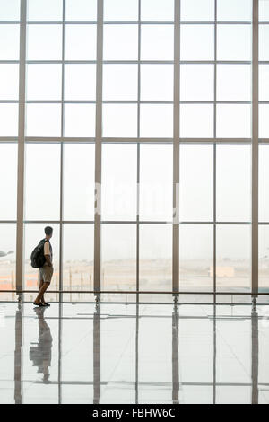 Minimalistic shot of full length silhouette of young handsome man with backpack waiting for flight, standing in modern airport t Stock Photo