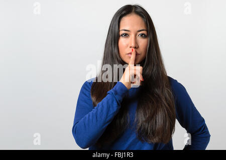 Pretty woman making a shushing gesture holding her finger to her lips as she asks for silence or to keep a secret Stock Photo