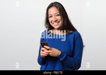 Smiling happy young woman with a confident friendly smile holding her mobile phone in her hand as she smiles at the camera, uppe Stock Photo