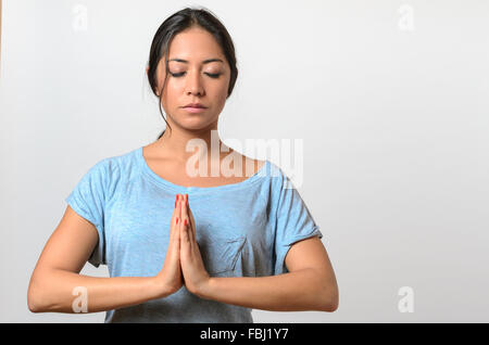 Young woman practicing yoga having her hands in front with a serene serious expression, upper body on white in a wellness and he Stock Photo