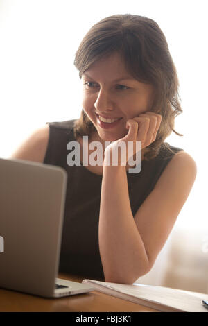 Friendly smiling young woman in formal wear using laptop, typing, working on computer, surfing internet Stock Photo