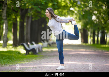 Beautiful sporty young woman working out in park alley, doing stretching exercise, standing in easy variation of Natarajasana, L Stock Photo