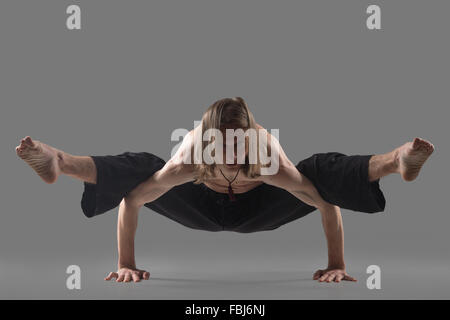 Sporty young man in black pants doing strengthening yoga pose, standing in arm balance, variation of Firefly posture, asana Titt Stock Photo