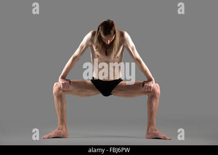 Sporty young yogi man doing strengthening yoga posture, standing in rudrasana (sumo), utkata konasana (goddess or temple pose), Stock Photo