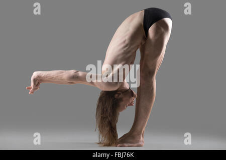 Sporty muscular young yogi man doing variation of Uttanasana posture with arms stretched behind the back, part of Surya Namaskar Stock Photo
