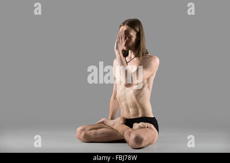 Sporty muscular young yogi man sitting cross-legged in lotus posture, padmasana, practicing Breathing technique Anuloma Viloma p Stock Photo