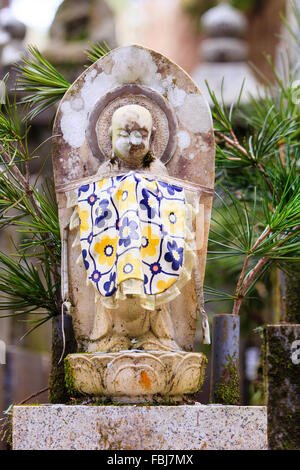 Japan, Koyasan, Okunoin cemetery. Blue and yellow bibbed Jizo Bosatsu stone statue, known as 'stone Buddha', on stone lotus blossom base. Stock Photo