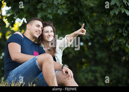 Beautiful happy young couple in love wearing casual clothes relaxing in park, enjoying the view, sitting together on grass on Stock Photo