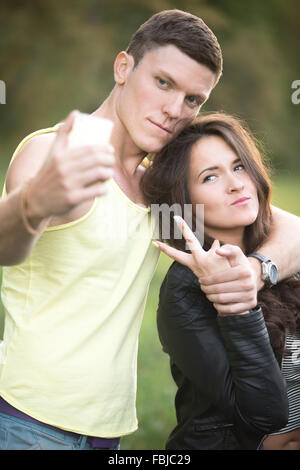 Young couple taking selfie portrait using mobile phone camera outdoors, smiling, hugging, posing, having fun together on summer Stock Photo