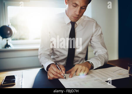 Executive male working at desk looking at documents and accounts holding a pen and looking concentrated and serious Stock Photo