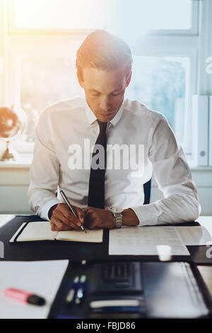 White male executive working at office at his desk with accounts and documents, looking in a black note book Stock Photo