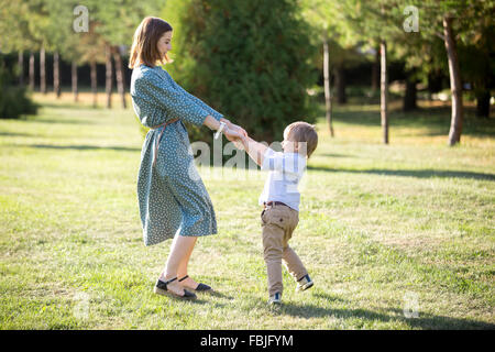 Portrait of happy young mom and her adorable little son playing and dancing together in park in summertime, smiling mother and k Stock Photo