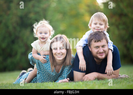 Mother, father and two kids lying on grass in park. Portrait of happy beautiful family of four relaxing on meadow, having fun to