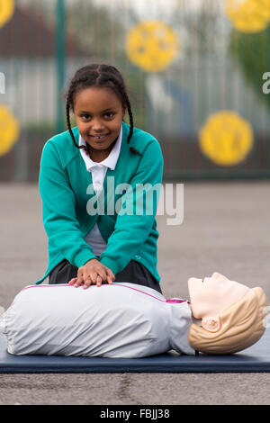 A schoolgirl learns life saving first aid techniques by practicing on a dummy at school. Stock Photo