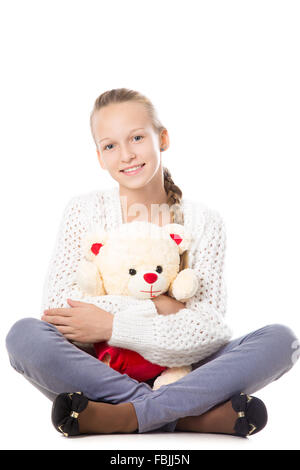 Portrait of happy beautiful casual teenage girl sitting cross-legged in knitted sweater hugging teddy bear, friendly smiling Stock Photo