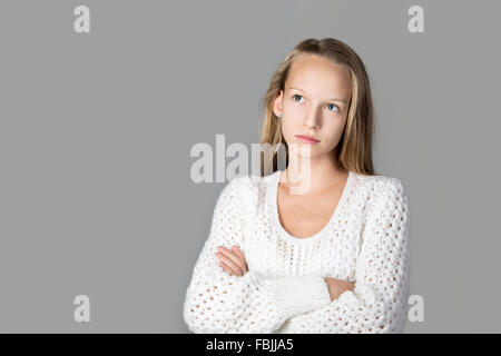 Portrait of beautiful pensive casual caucasian teenage girl wearing knitted sweater, studio image, gray background Stock Photo