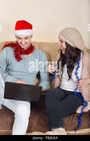 Happy Couple Looking Winter Vacation Destinations on Laptop, Christmas Time. Young Attractive Couple with Santa Hat Together in  Stock Photo