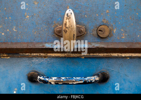 Closeup of the lid of a rusty blue metal tool box. The two worn handles and the key hole form a smiling face Stock Photo