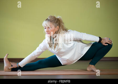 Sporty beautiful blond young woman working out indoors, doing asana for strengthening and stretching shoulders, spine, groins Stock Photo