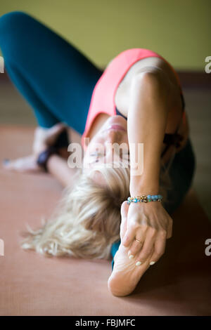 Sporty beautiful blond young woman working out indoors, doing posture for strengthening and stretching shoulders, spine, groins Stock Photo