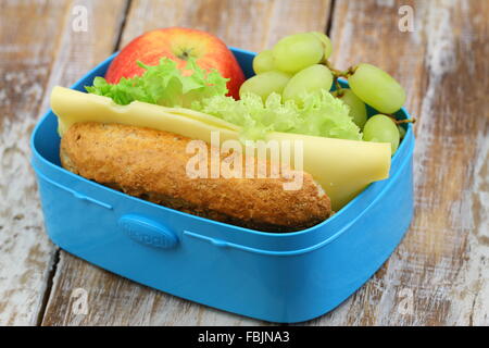 Healthy lunch box containing brown bread roll with cheese and lettuce, red apple and grapes Stock Photo
