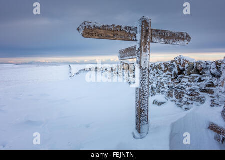 Pen-y-ghent summit in winter snow; the signpost for the Pennine Way and Horton-in-Ribblesdale iced up. Yorkshire Dales. Stock Photo