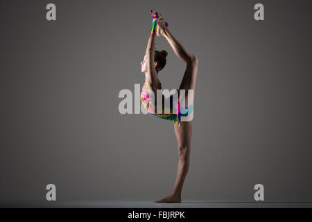 Beautiful cool young fit gymnast woman in colorful sportswear working out, standing on one leg, performing back scale Stock Photo