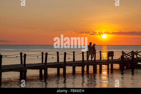 couple enjoying romantic walk on pier by ocean during sunset Stock Photo