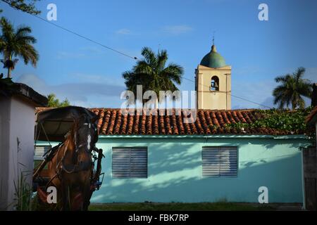 rural Vinales church with bell tower and palm trees rising above the tiled roof, with a pony and trap waiting patiently outside Stock Photo