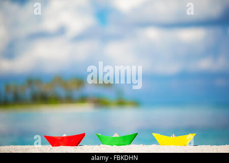 Business concept for challenge and movement: three colorful paper boats on turquoise ocean background. Green, red and yellow paper boats on tropical white beach outdoors Stock Photo
