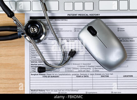 Patient medical history form with stethoscope, computer keyboard and mouse on wooden desktop. Stock Photo