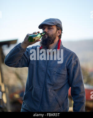 Young farmer drinking a bottle of beer in the courtyard Stock Photo
