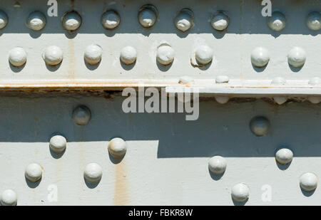 Close-up of rivets on painted steel surface with some rust stains, partly casting shadows from top. Stock Photo
