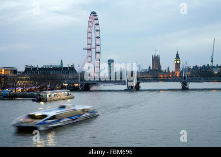 Big Ben Houses of Parliament and London Eye view from Waterloo Bridge at night with boat moving on river Stock Photo