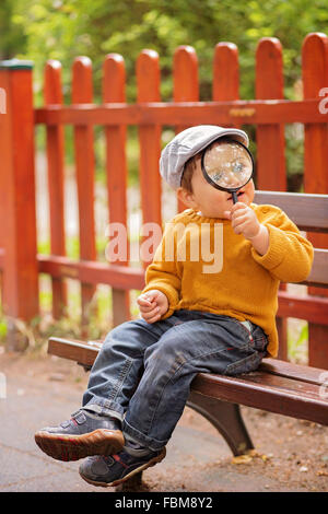 Boy sitting on bench holding a magnifying glass Stock Photo